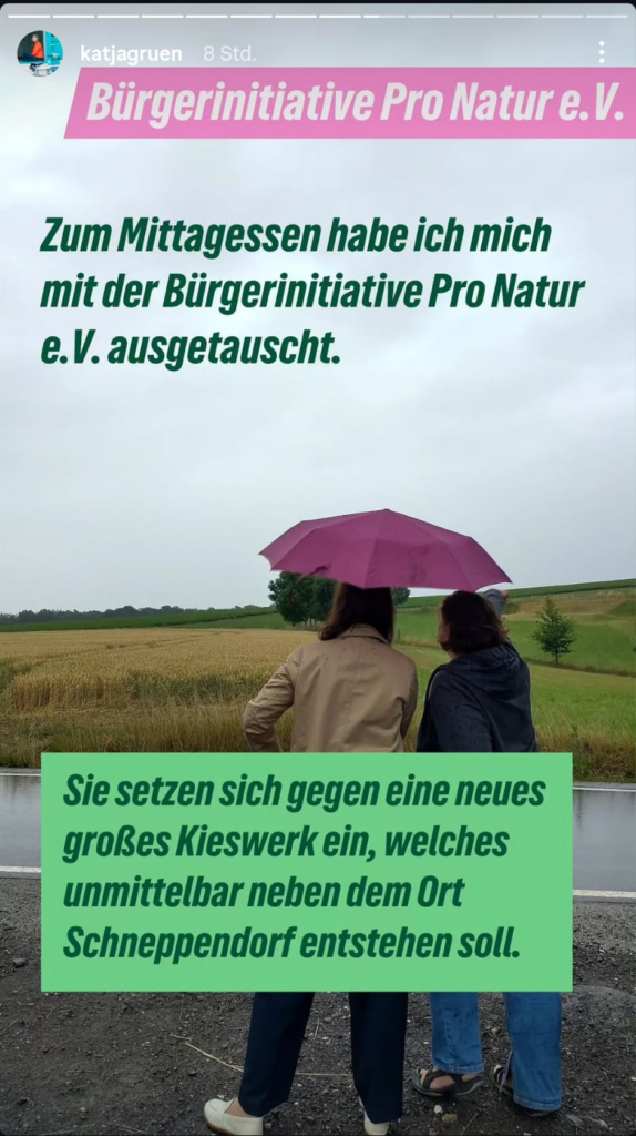 Screenshot einer Instagram-Story von Katja Meier: Zwei Frauen stehen von hinten gesehen unter einem pinkfarbenen Regenschirm am Straßenrand und blicken auf Felder bei Schneppendorf. Eingeblendeter Text: „Zum Mittagessen habe ich mich mit der Bürgerinitiative Pro Natur e.V. ausgetauscht. Sie setzen sich gegen ein neues großes Kieswerk ein, welches unmittelbar neben dem Ort Schneppendorf entstehen soll.“